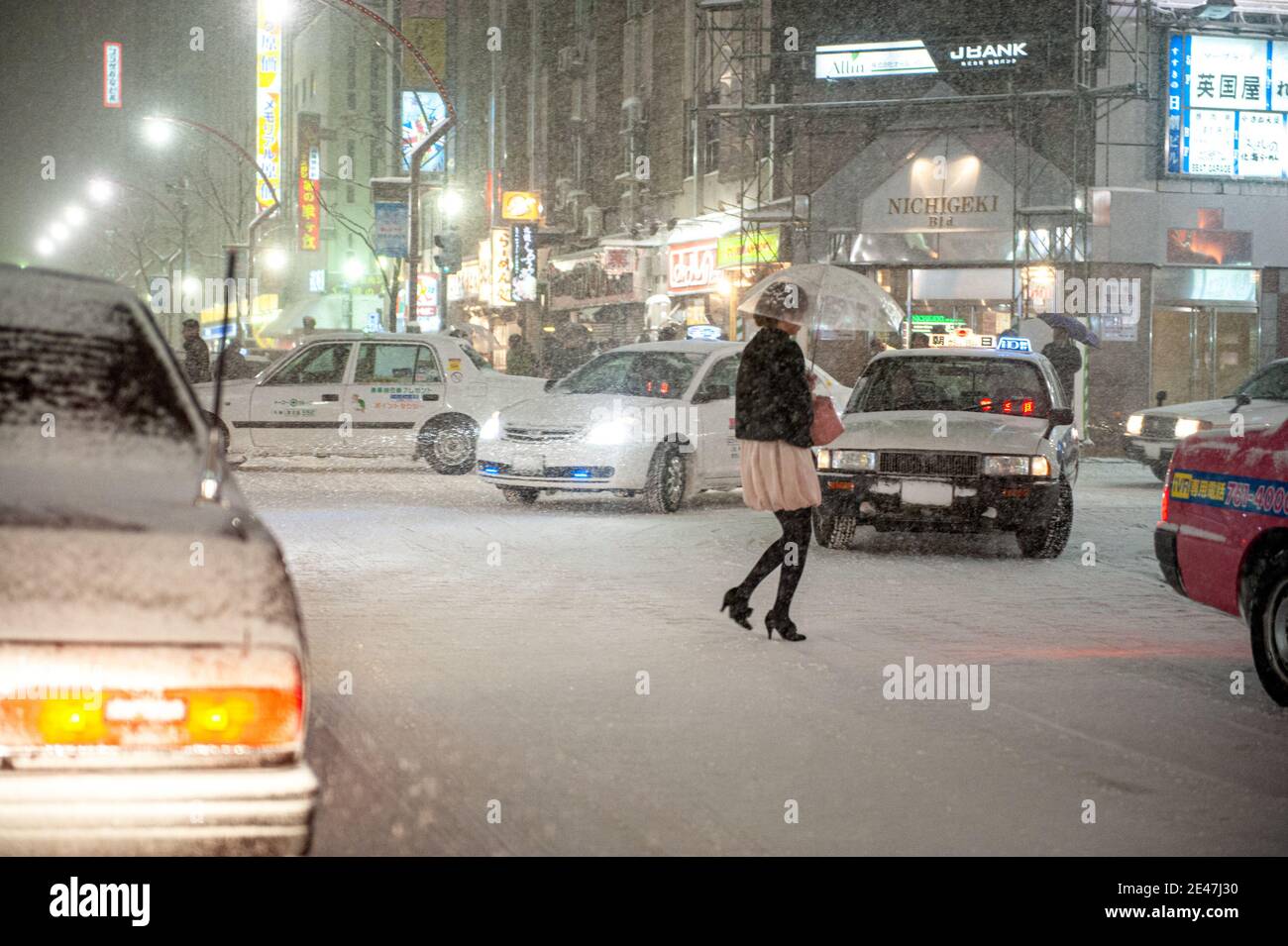 Une femme qui marche dans une rue animée et enneigée pendant une tempête de neige dans une ville japonaise. Banque D'Images