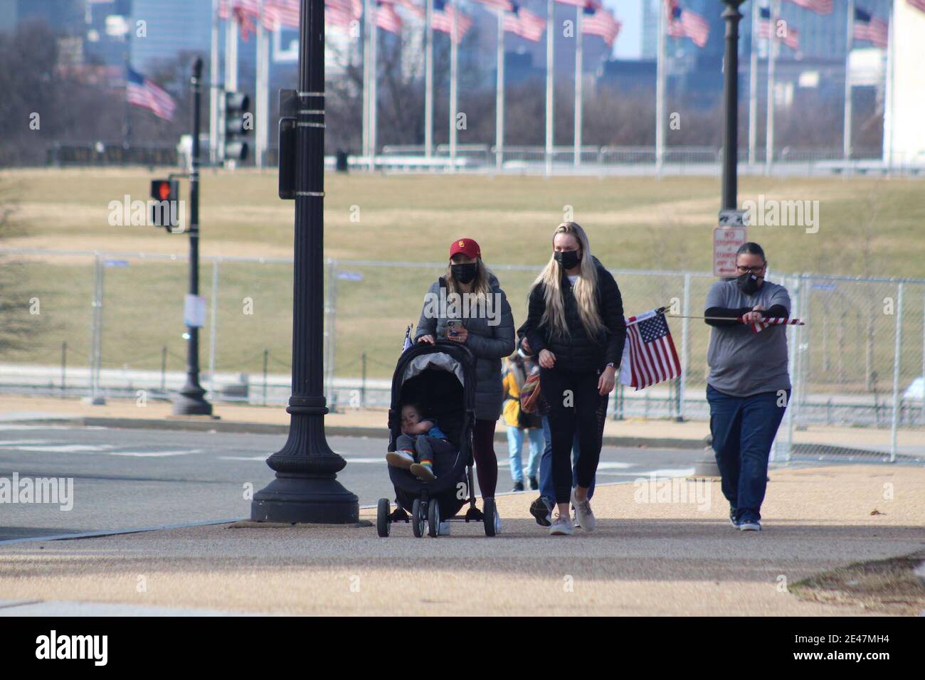Washington DC, District de Columbia, États-Unis. 21 janvier 2021. Le lendemain de l'assermentation de Joe Biden, le National Mall toujours entouré de clôtures métalliques s'est ouvert aux visiteurs, leur permettant même de prendre des drapeaux. Cette famille à visage masqué marche des drapeaux suspendus vers le parc où près de 200,000 petits drapeaux ont été plantés en hommage aux victimes décédées de Covid-19. Le parc a également donné un effet impressionnant après avoir été illuminé pendant les cérémonies d'inauguration. Crédit : Marie le BLE/ZUMA Wire/Alay Live News Banque D'Images