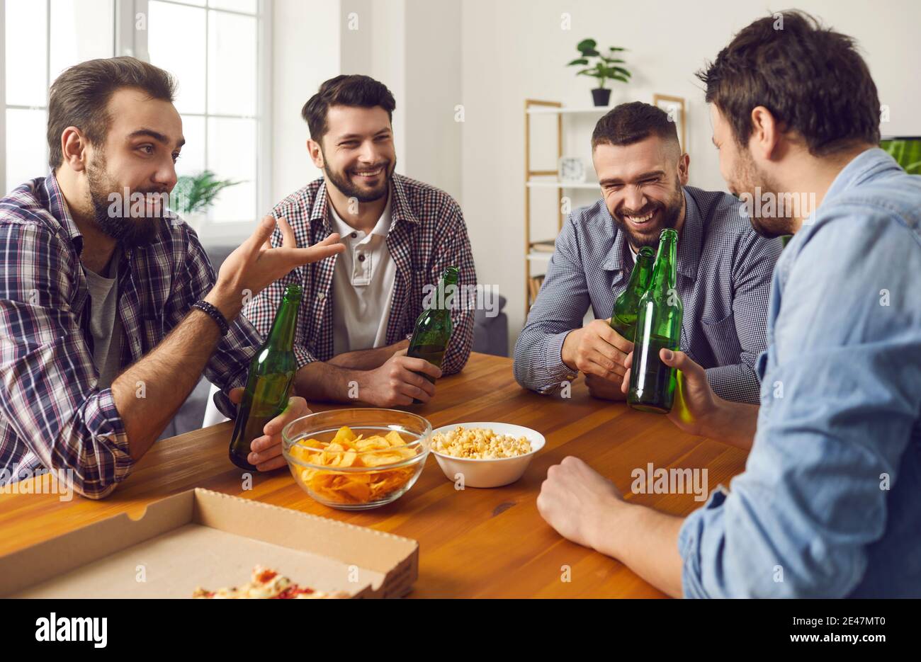 Groupe d'hommes souriants amis assis avec des bouteilles d'ours et en-cas et discussions Banque D'Images