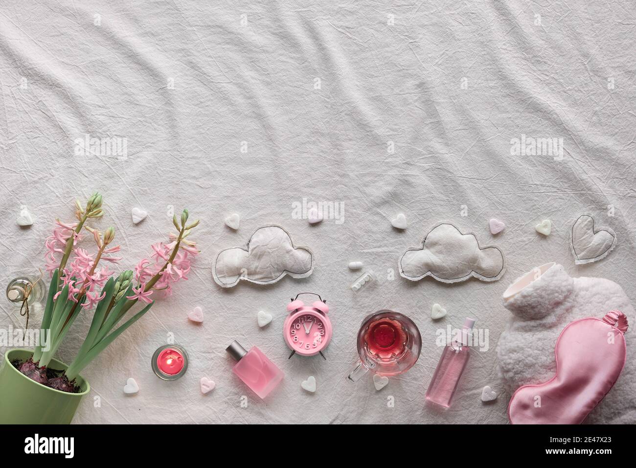 Concept créatif de sommeil sain. Fond blanc cassé en tissu ivoire. Fleurs de jacinthe roses, alarme, huile essentielle rose. Oreiller orthopédique, sommeil Banque D'Images
