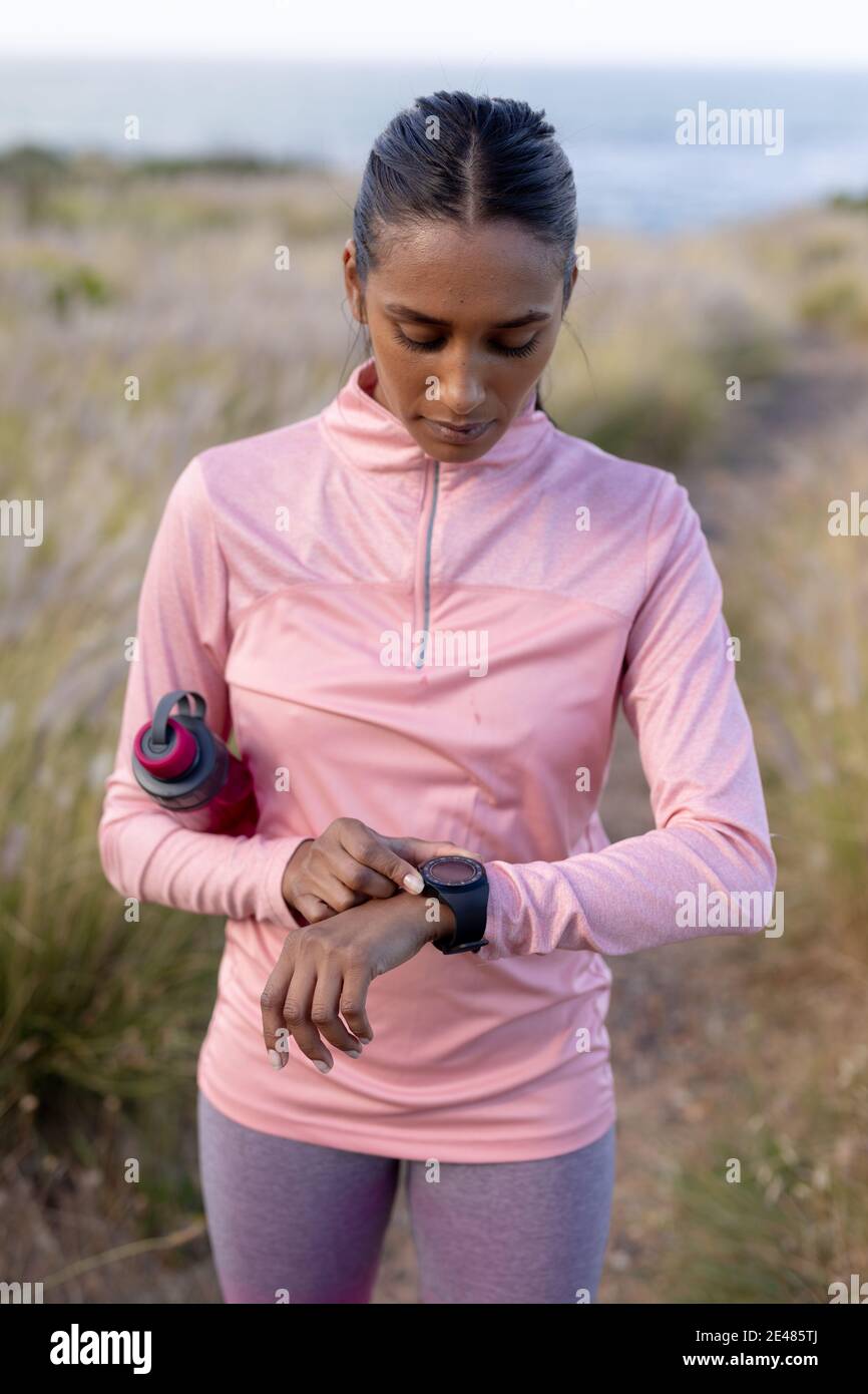 Portrait d'une femme afro-américaine en tenue sportive avec une montre intelligente tenir l'eau dans l'herbe haute Banque D'Images