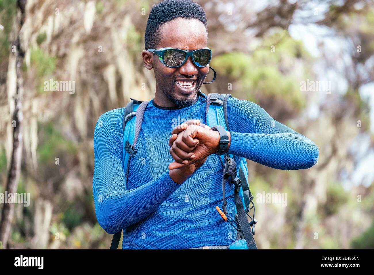 Portrait d'un jeune homme d'origine ethnique afro-américaine souriant en train de vérifier un corbillard ou une distance sur la montre à bracelet dans la forêt pendant un hiki Banque D'Images