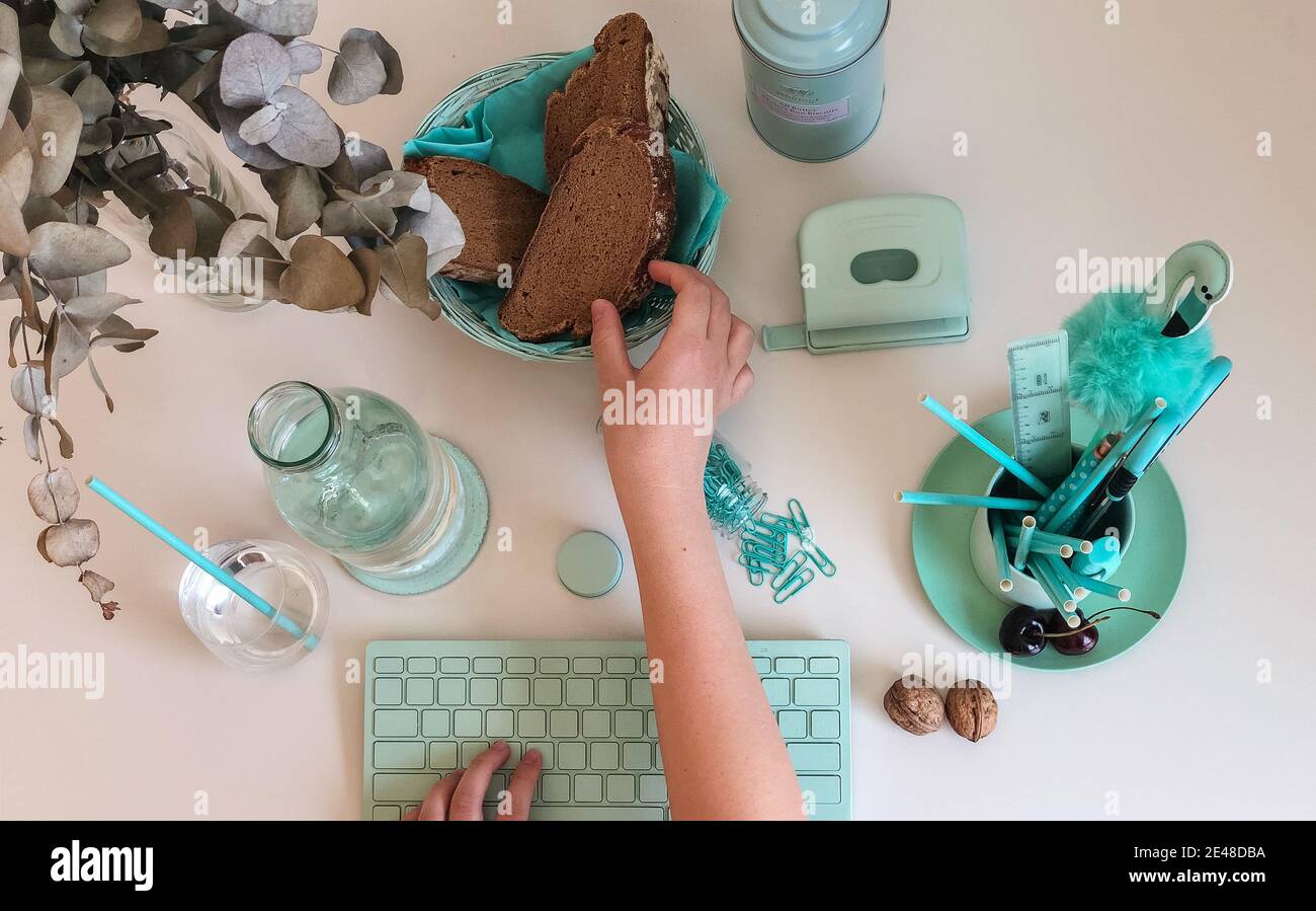 PETRER, ESPAGNE - 17 juillet 2019: Différents objets de couleur turquoise comme un clavier d'ordinateur, des stylos et des trombones; et saisir à la main un morceau de pain Banque D'Images