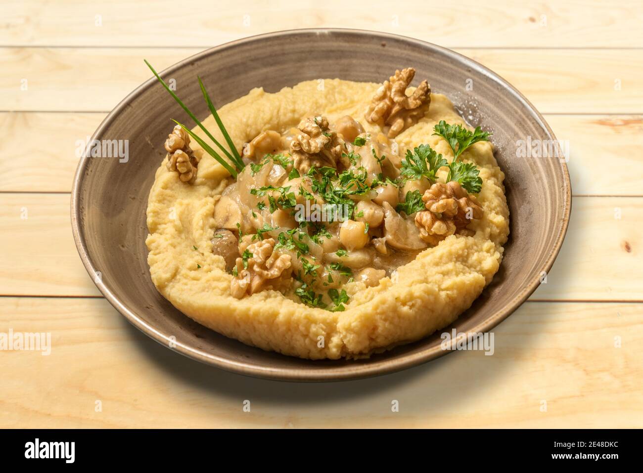 Houmous au persil, à l'huile d'olive et aux noix. Crème israélienne de pois chiches dans un bol en faïence sur une table en bois Banque D'Images
