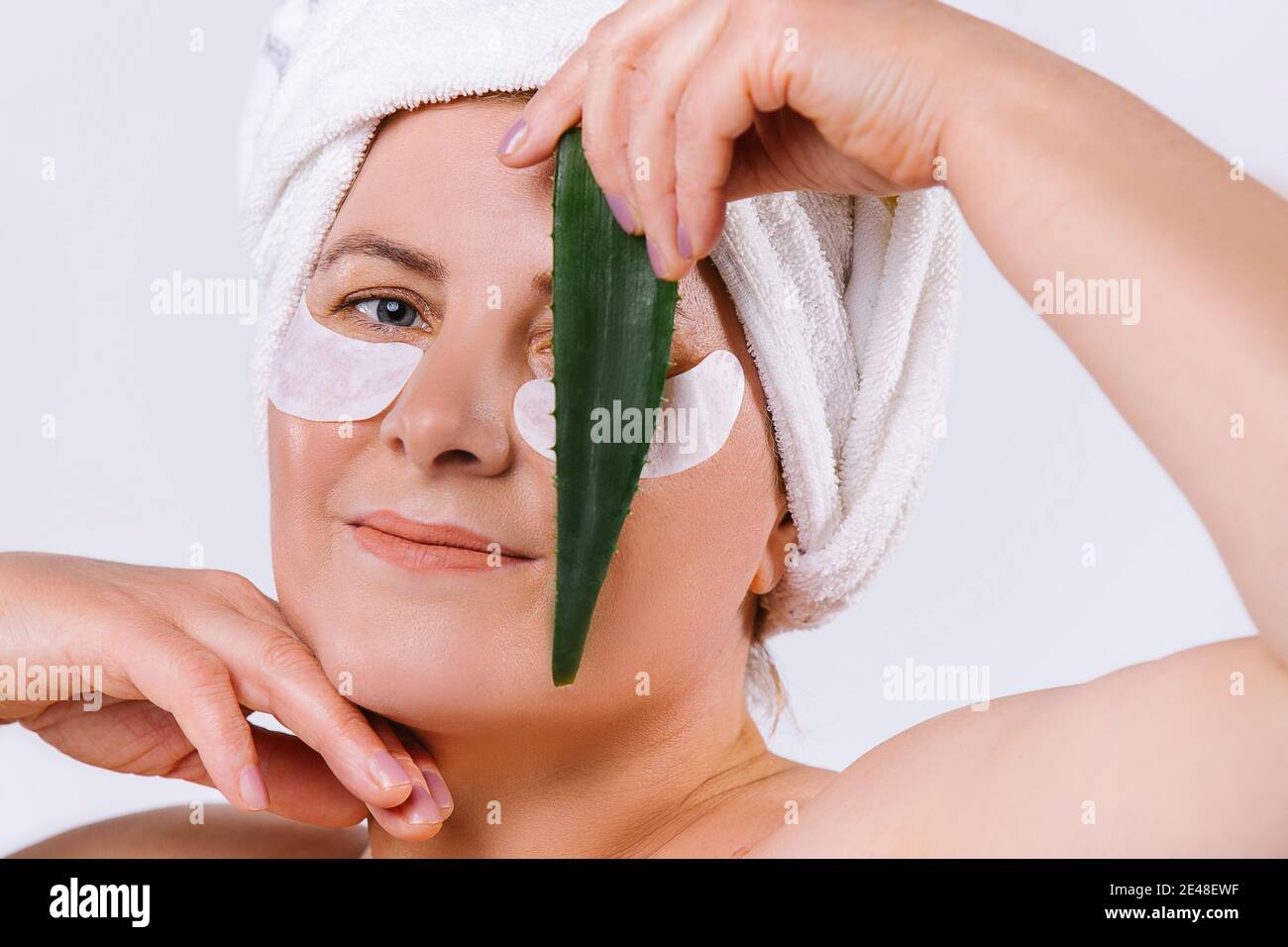 Portrait d'une femme âgée de race blanche avec une peau équitable, des taches cosmétiques pour les yeux et une feuille d'aloe vera devant le visage, fermant un œil. Arrière-plan blanc. Banque D'Images