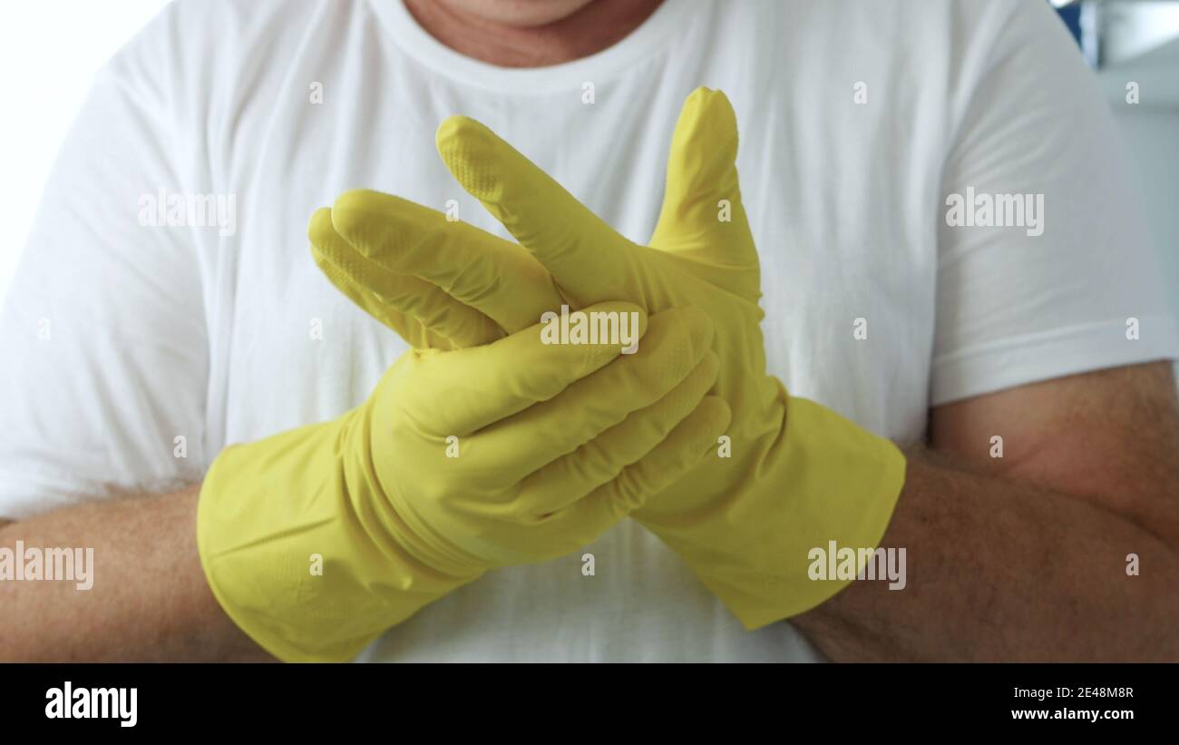 L'homme met ses gants de protection jaunes sur ses mains en préparation Pour commencer le nettoyage dans la cuisine et la salle de bains Banque D'Images