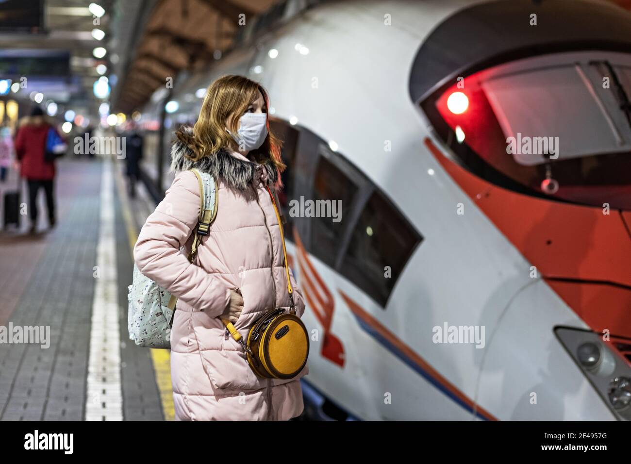 Une jeune femme dans un masque médical se tient sur la plate-forme de la gare, attendant le départ d'un train à grande vitesse. La pandémie du coronavirus Banque D'Images