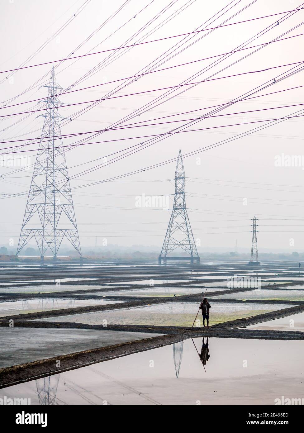 MUMBAI, INDE - 17 décembre 2020 : ouvriers non identifiés dans une ferme de sel de mer et une grange avec des lignes électriques haute tension en arrière-plan Banque D'Images