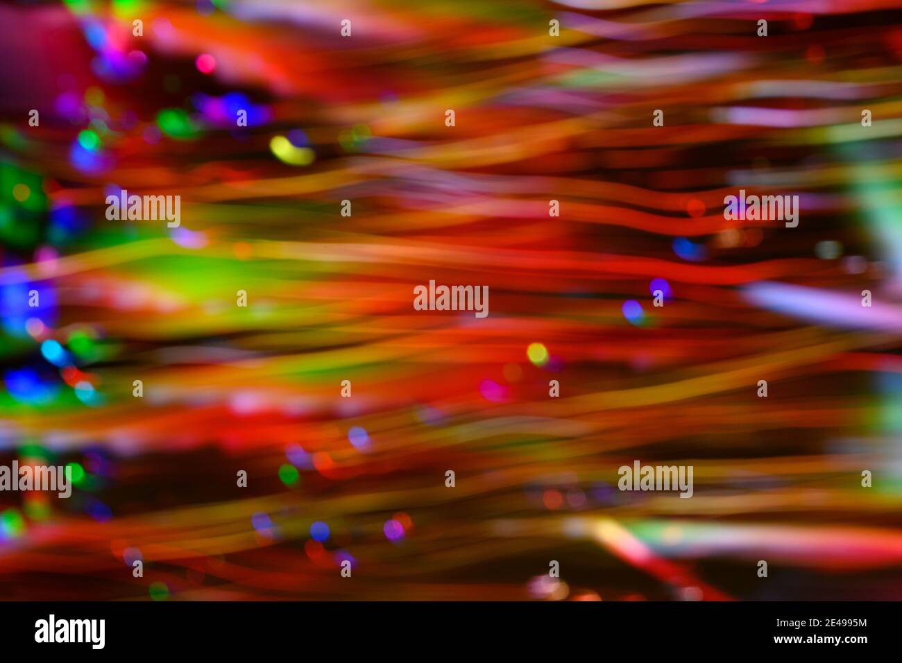 Points défocurés et tendrils horizontaux de couleur rouge, vert, bleu et jaune créés par des lumières LED photographiées à l'extérieur la nuit. Banque D'Images