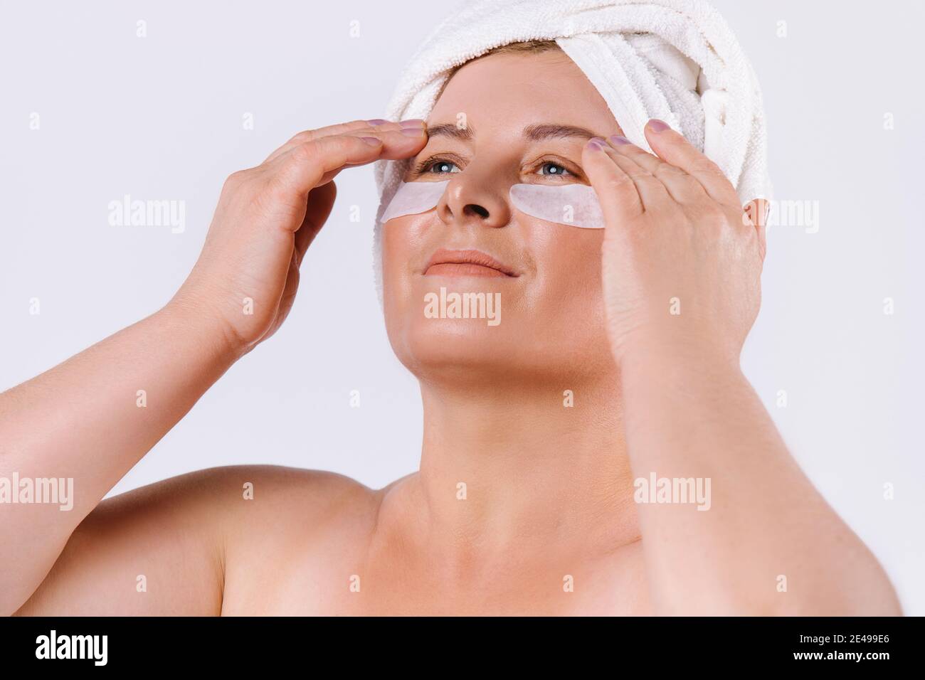 Une photo agrandie d'une femme âgée à la peau équitable avec une serviette blanche sur sa tête et des taches sous ses yeux regardant sur un fond blanc Banque D'Images