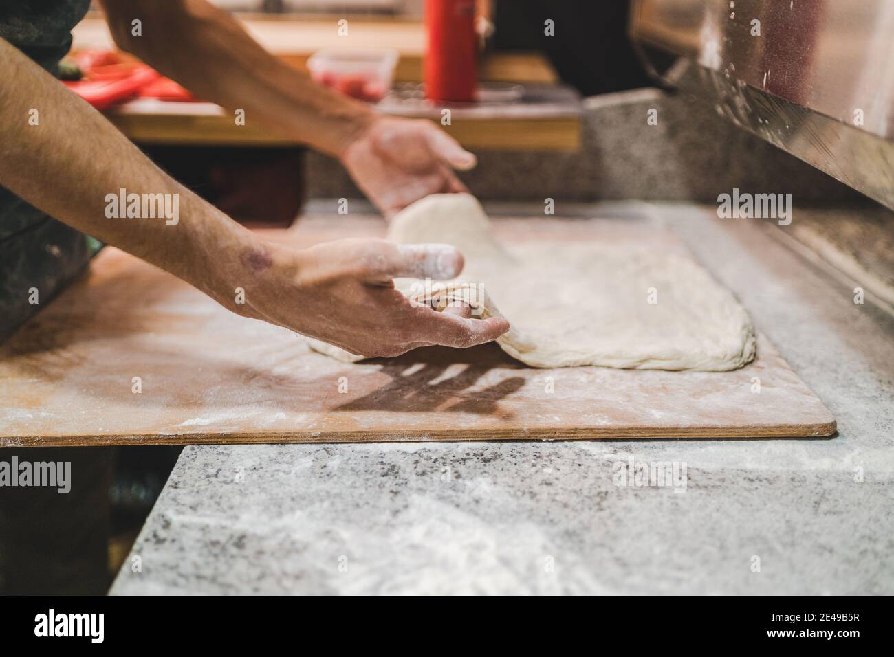 Chef façonnant la pâte à pizza sur une planche de bois, vue latérale Banque D'Images