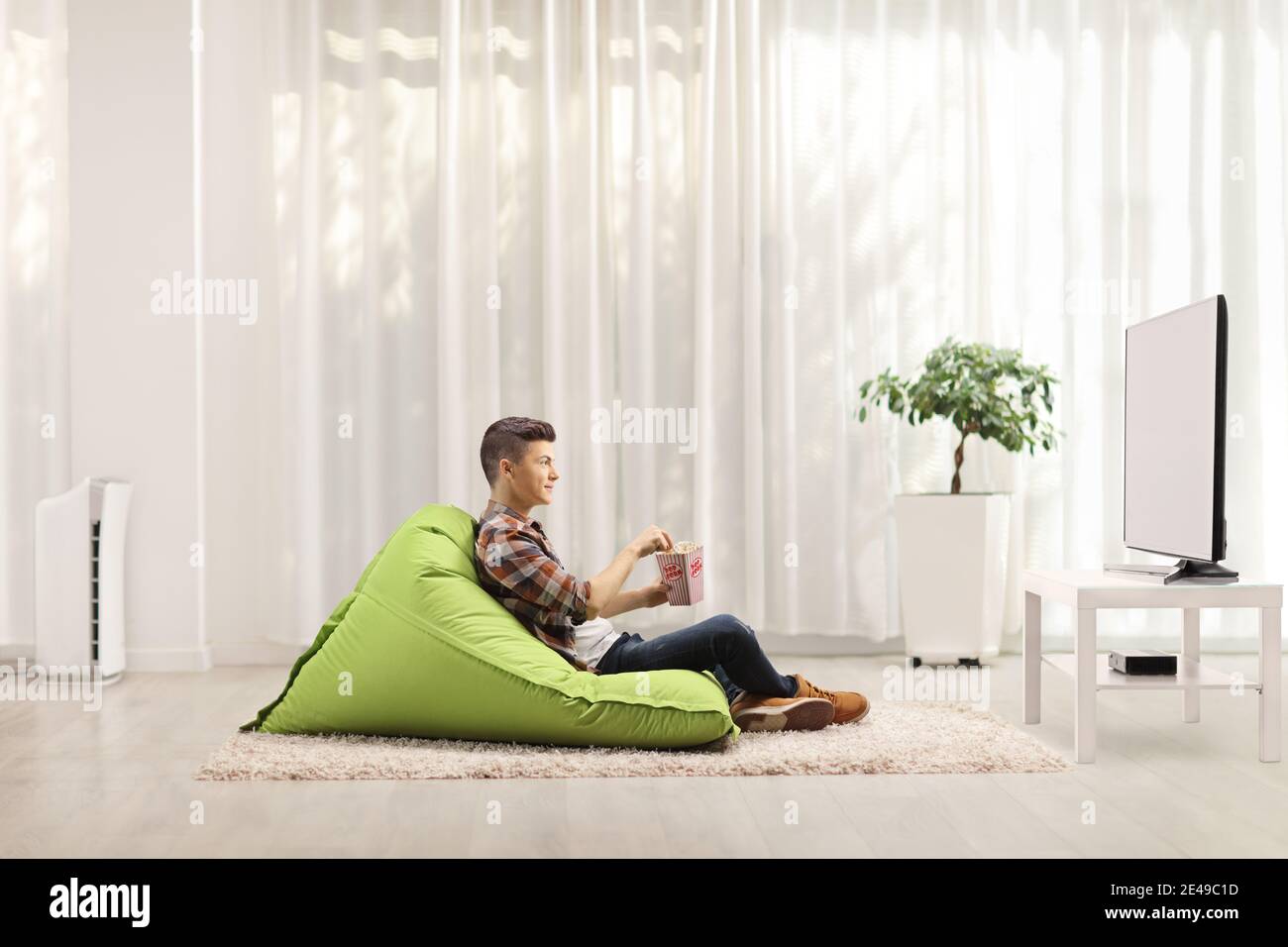 Adolescent de sexe masculin assis sur un fauteuil de sac de haricots avec  un boîte de pop-corn et regarder la télévision dans un cadre minimaliste et  moderne séjour Photo Stock - Alamy