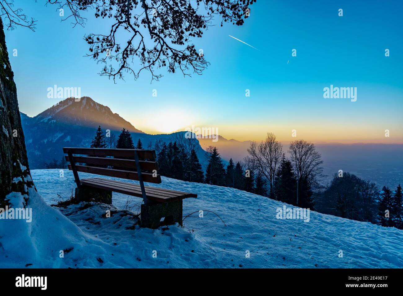 Die letzten Sonnenstrahlen leuchten über den Karren auf eine Parkbank unter einem Baum. Coucher de soleil avec banc, arbre. Banque D'Images