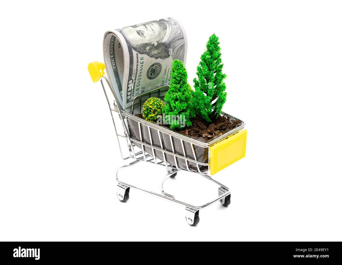Gros plan d'un chariot à jouets avec terre, arbres à jouets et billets de dollars isolés sur blanc. Concept de préservation des forêts et de prévention de la déforestation. Banque D'Images