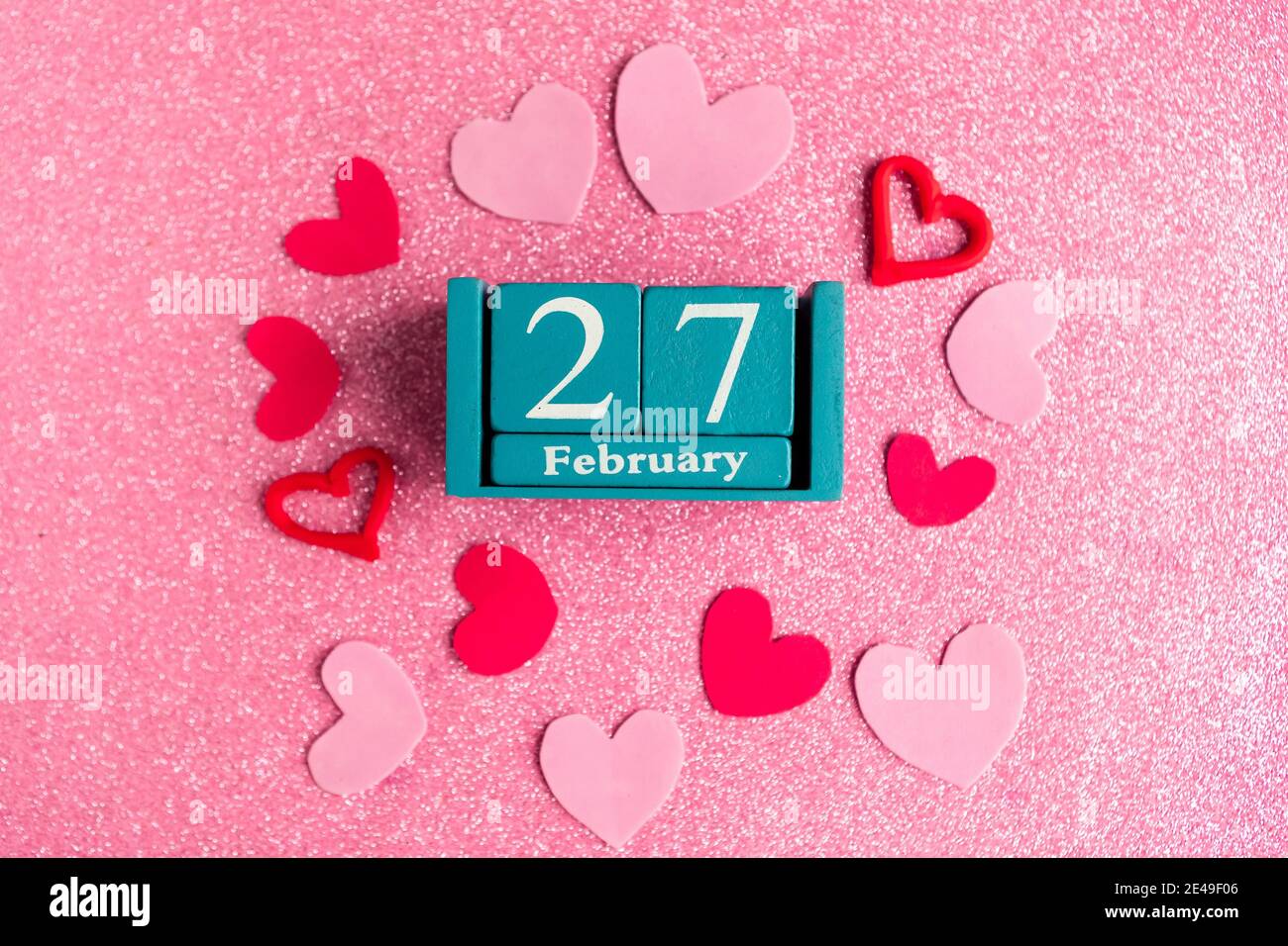 Février 27. Calendrier cube bleu avec mois et date et décorations sur fond rose scintillant. Banque D'Images