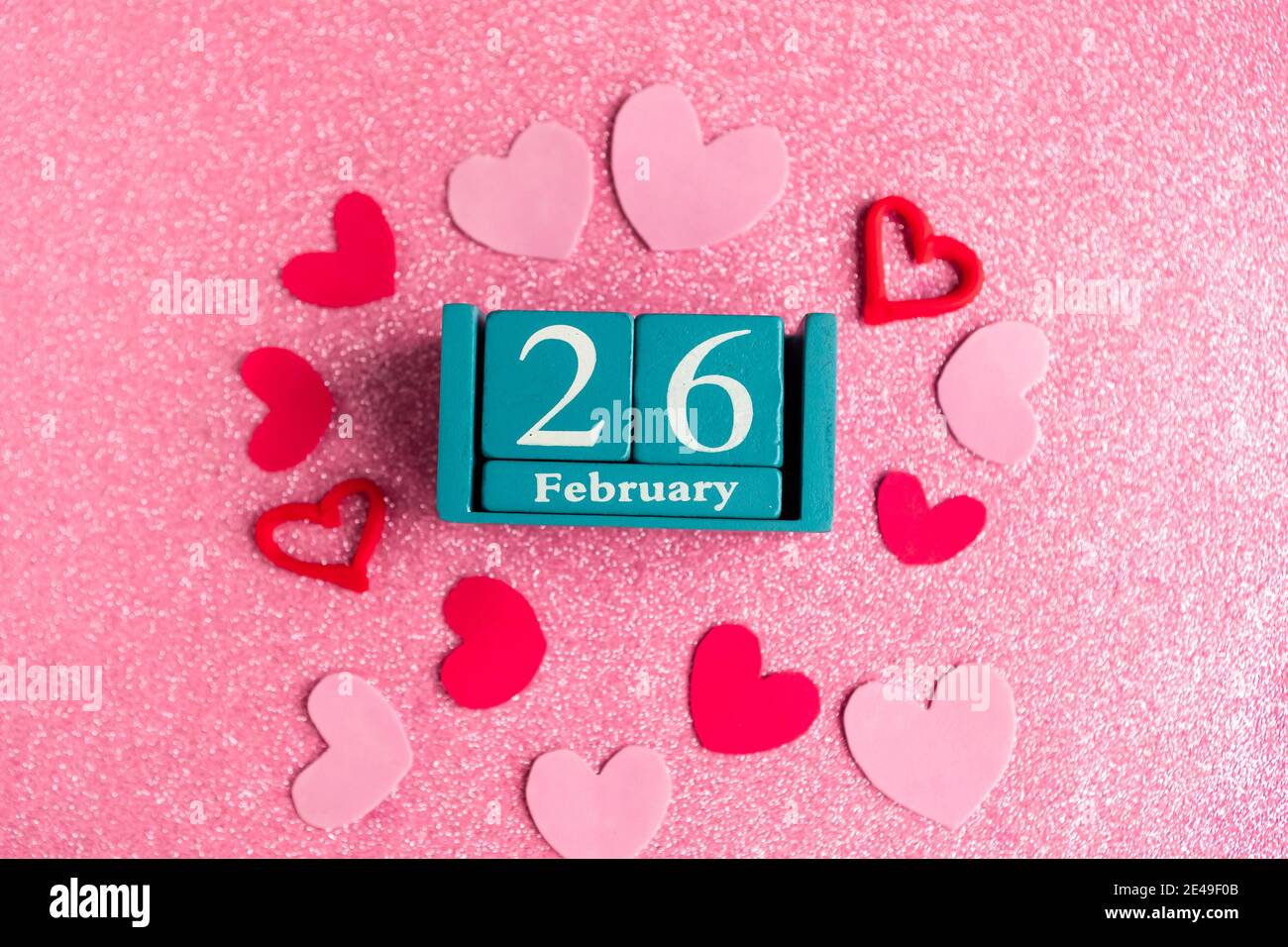 Février 26. Calendrier cube bleu avec mois et date et décorations sur fond rose scintillant. Banque D'Images