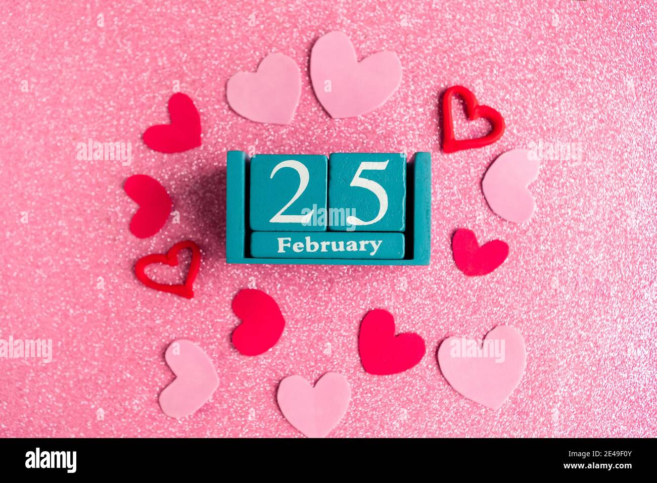 Février 25. Calendrier cube bleu avec mois et date et décorations sur fond rose scintillant. Banque D'Images