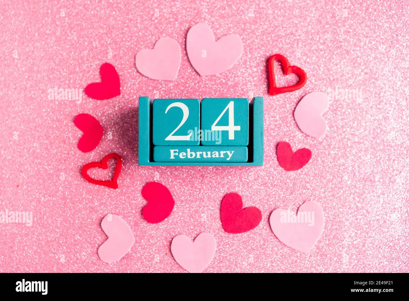 Février 24. Calendrier cube bleu avec mois et date et décorations sur fond rose scintillant. Banque D'Images