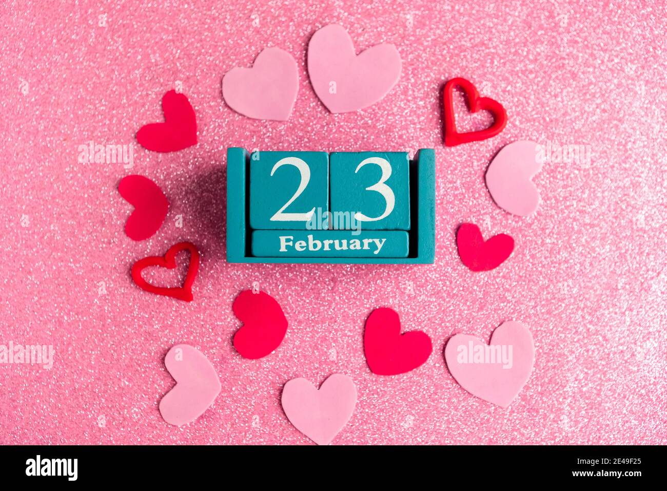 Février 23. Calendrier cube bleu avec mois et date et décorations sur fond rose scintillant. Banque D'Images