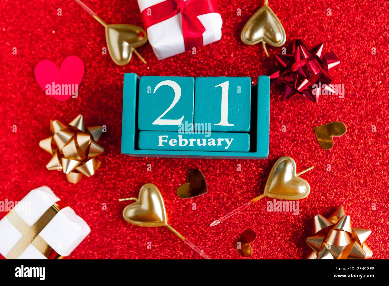 Février 21. Calendrier cube bleu avec mois et date et décorations sur fond rouge pailleté. Banque D'Images