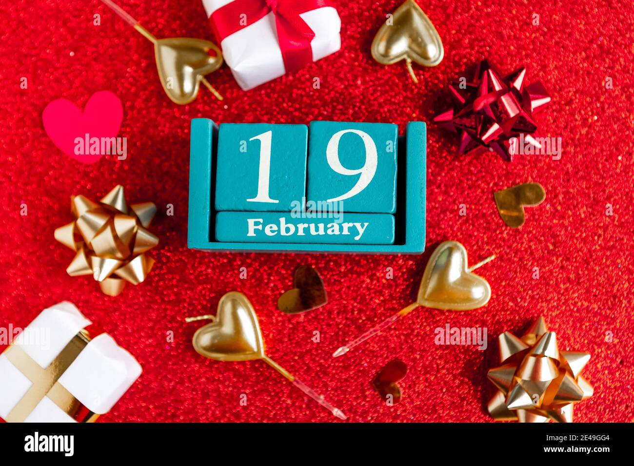 Février 19. Calendrier cube bleu avec mois et date et décorations sur fond rouge pailleté. Banque D'Images