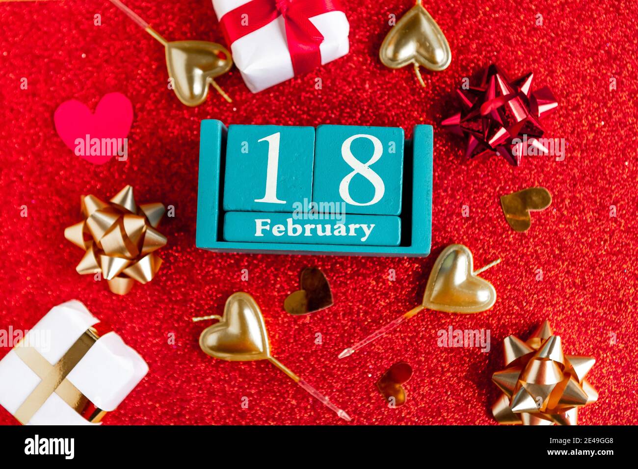 Février 18. Calendrier cube bleu avec mois et date et décorations sur fond rouge pailleté. Banque D'Images