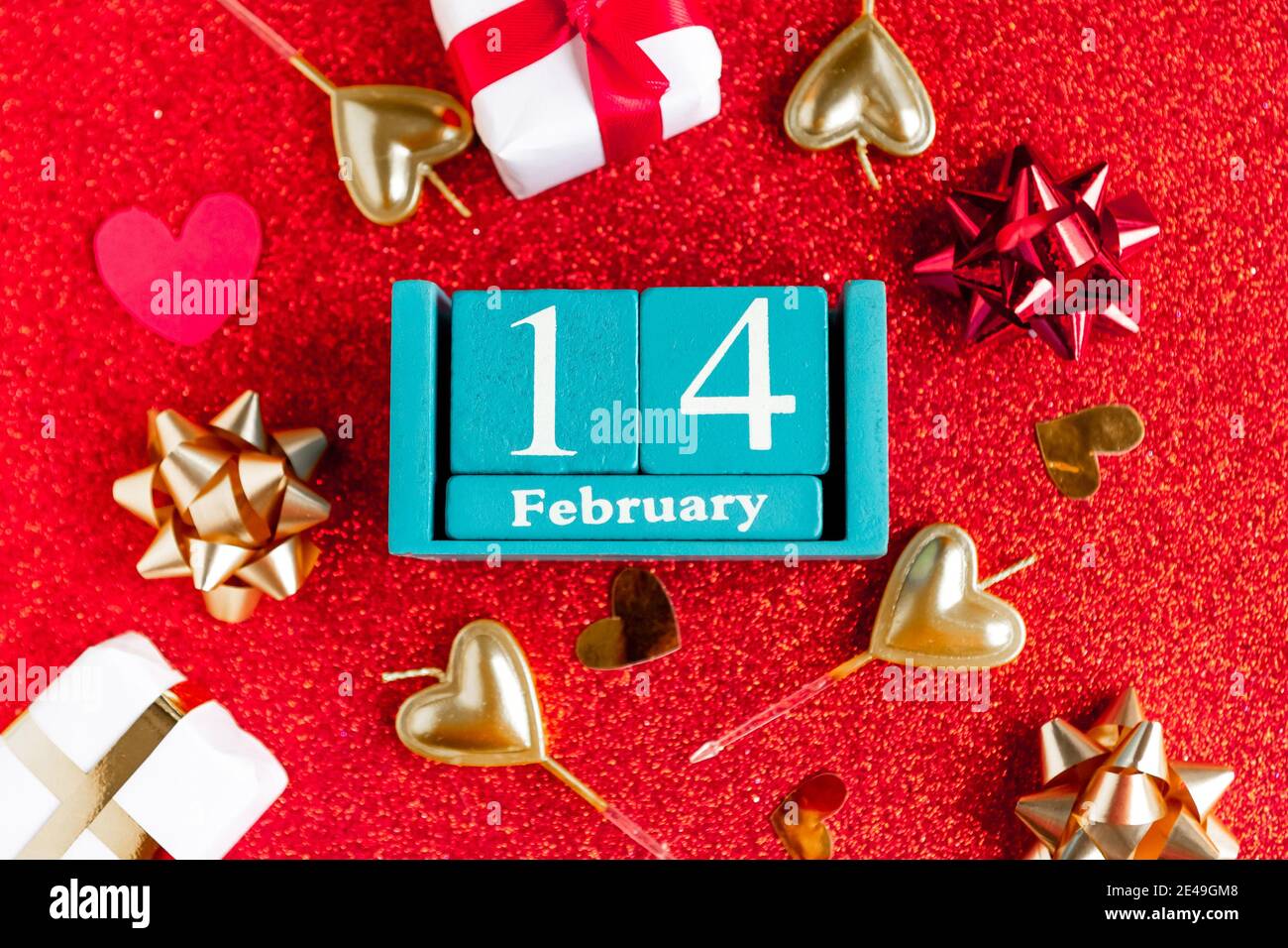 Février 14. Calendrier cube bleu avec mois et date et décorations sur fond rouge pailleté. Banque D'Images