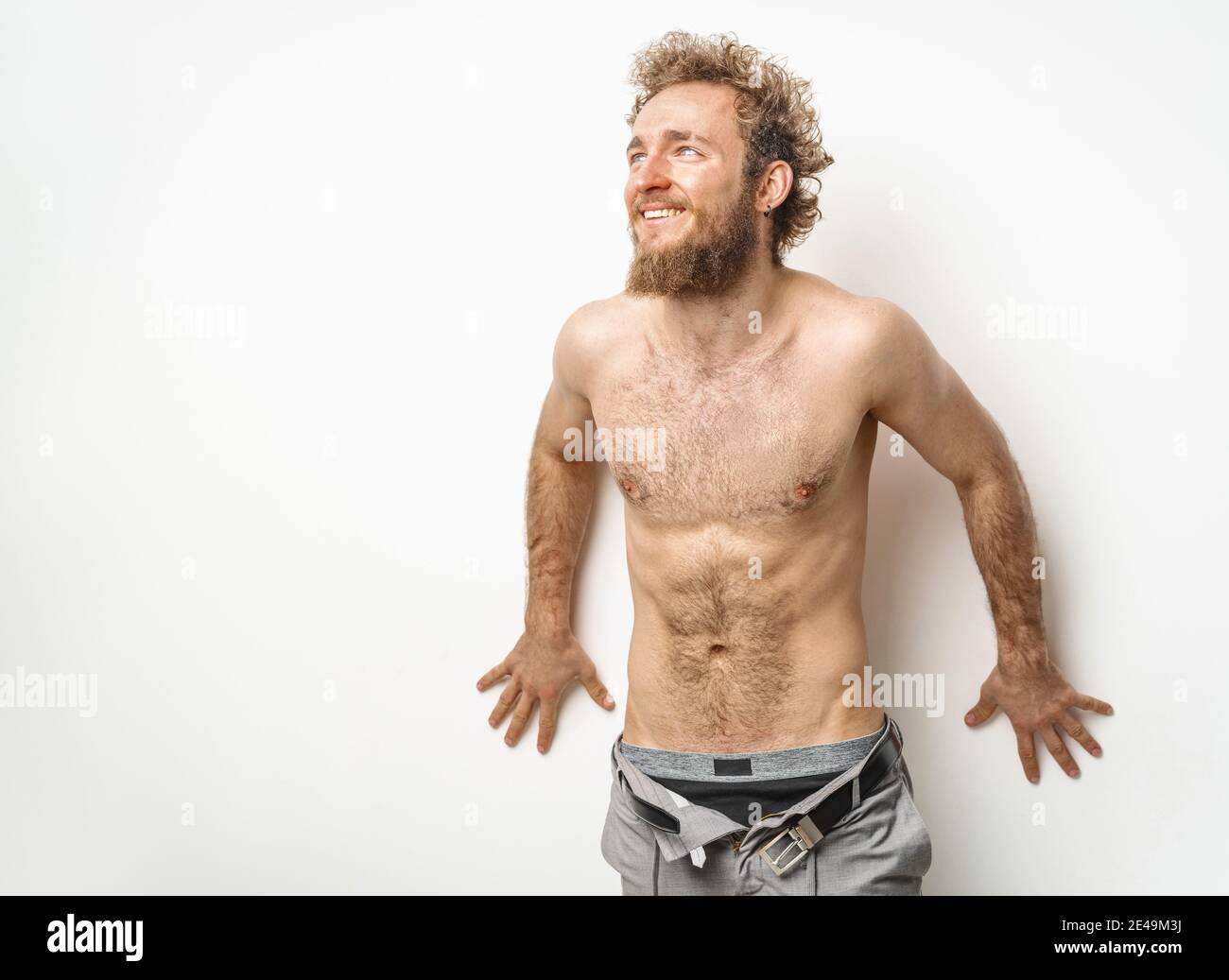 Un beau shirless tatoué jeune homme avec la barbe et les cheveux bouclés porter un jean en denim non boutonné avec des sous-vêtements à l'aspect latéral isolé sur blanc Banque D'Images