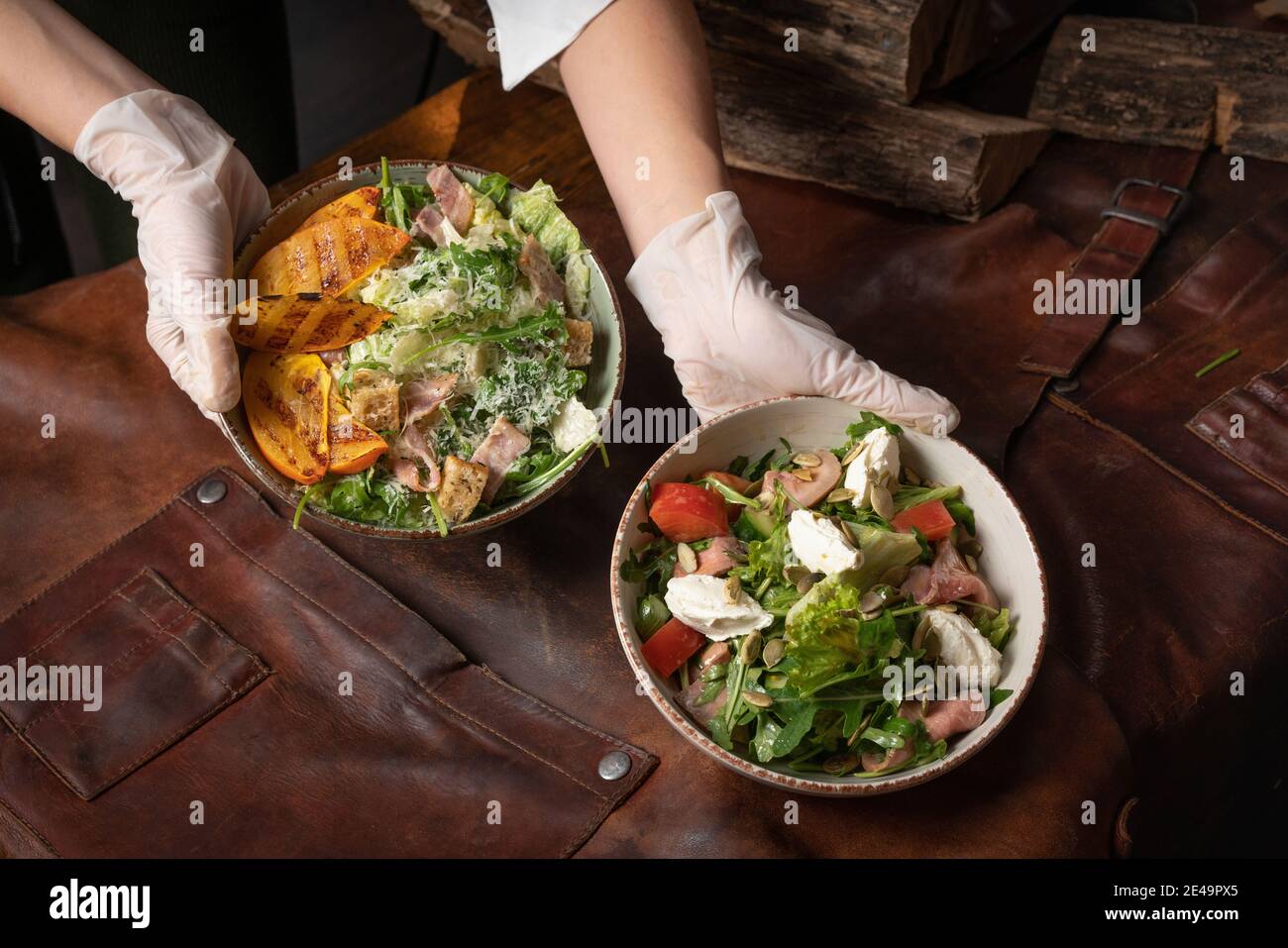 Deux mains avec des bols de salade de légumes avec du saumon, du fromage mozzarella et des tranches de fruits grillées se dressent sur une table recouverte d'un chiffon en cuir Banque D'Images