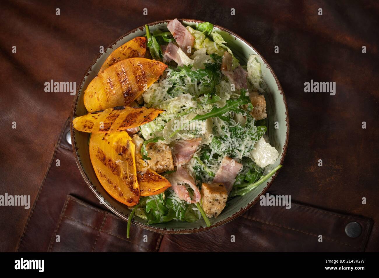 Vue de dessus d'un bol de salade fraîche avec du saumon, de la mozzarella et des tranches de fruits grillées se dresse sur une table recouverte d'un chiffon en cuir. Restaurant Banque D'Images