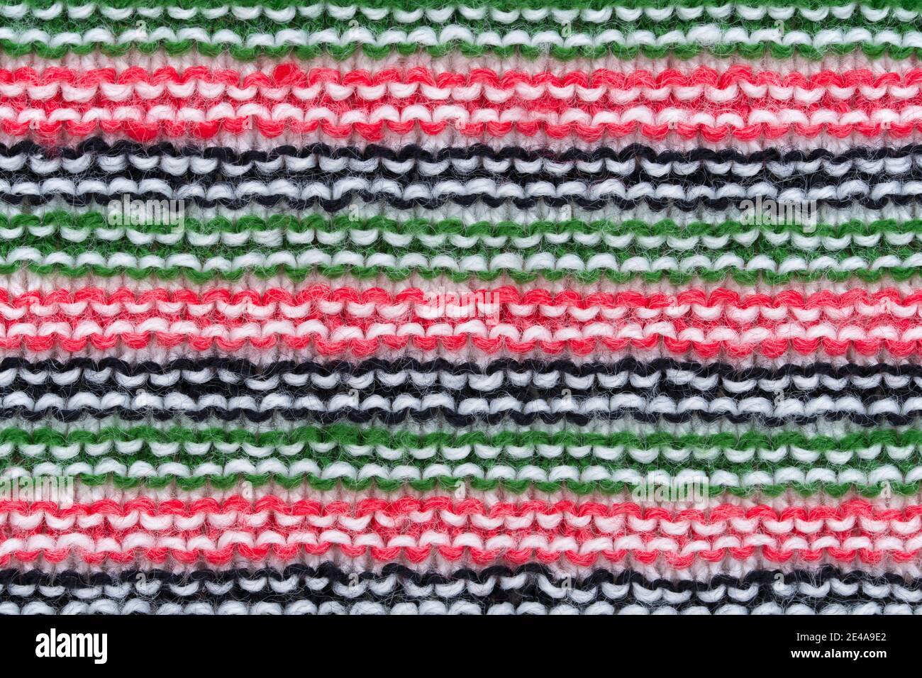Gros plan sur un motif en laine tricotée fait à la main en rouge, blanc, noir et vert. Banque D'Images