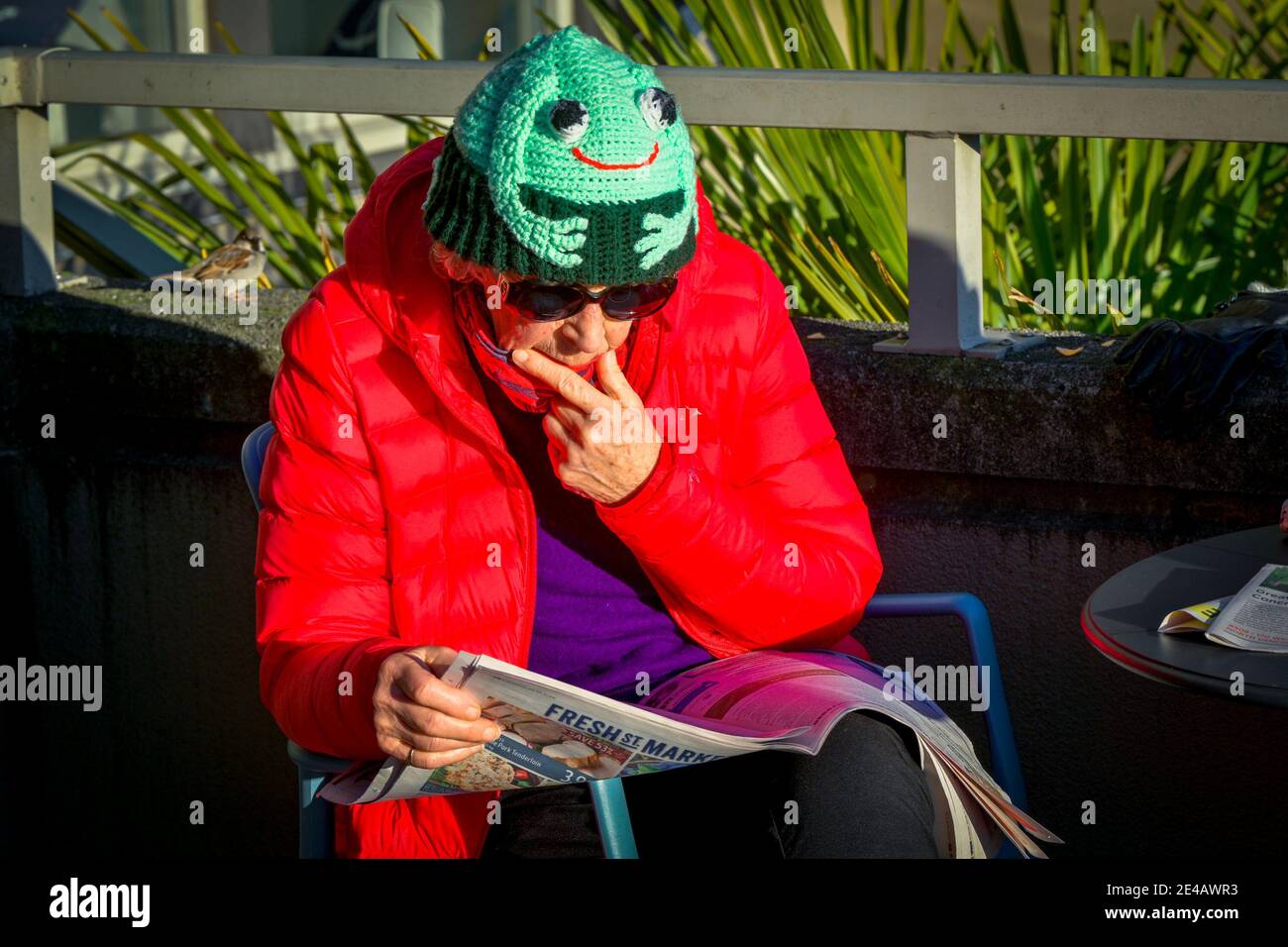 Femme âgée lisant des journaux, portant un chapeau de grenouille. Banque D'Images
