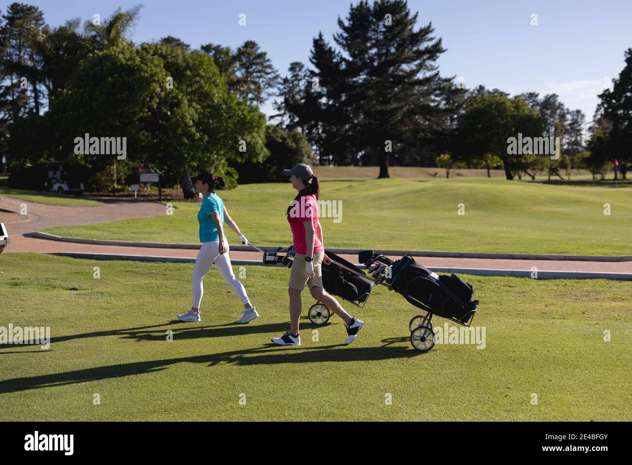Deux femmes de race blanche marchant sur le parcours de golf tirant des sacs de golf sur roues Banque D'Images