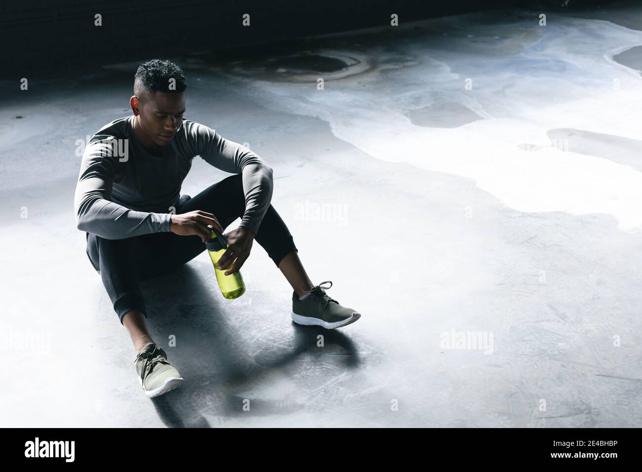 Homme afro-américain assis dans un bâtiment urbain vide et reposant après avoir joué au basket-ball Banque D'Images