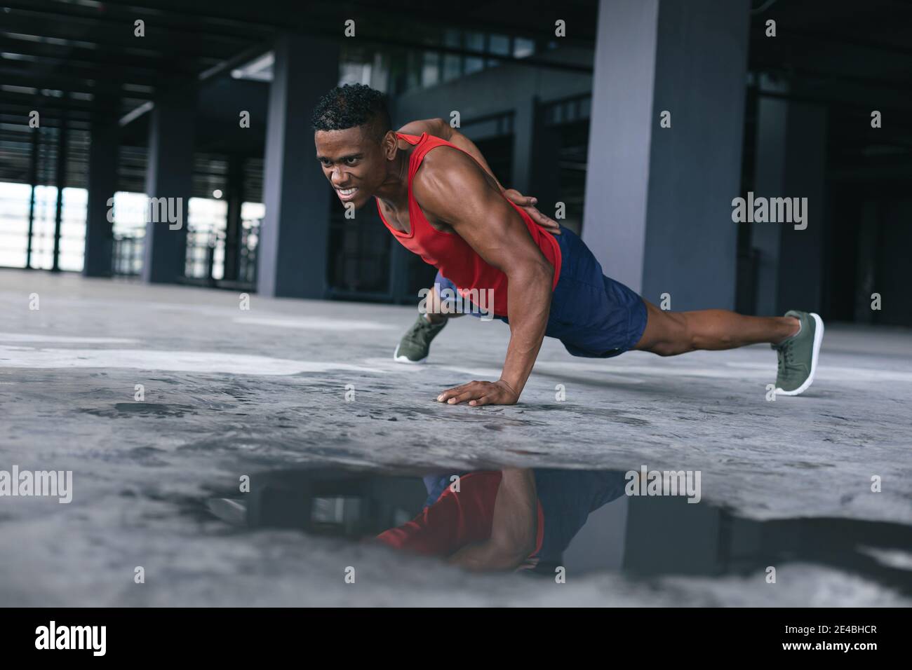 Homme afro-américain portant des vêtements de sport faisant une pression d'une main ups dans un bâtiment urbain vide Banque D'Images