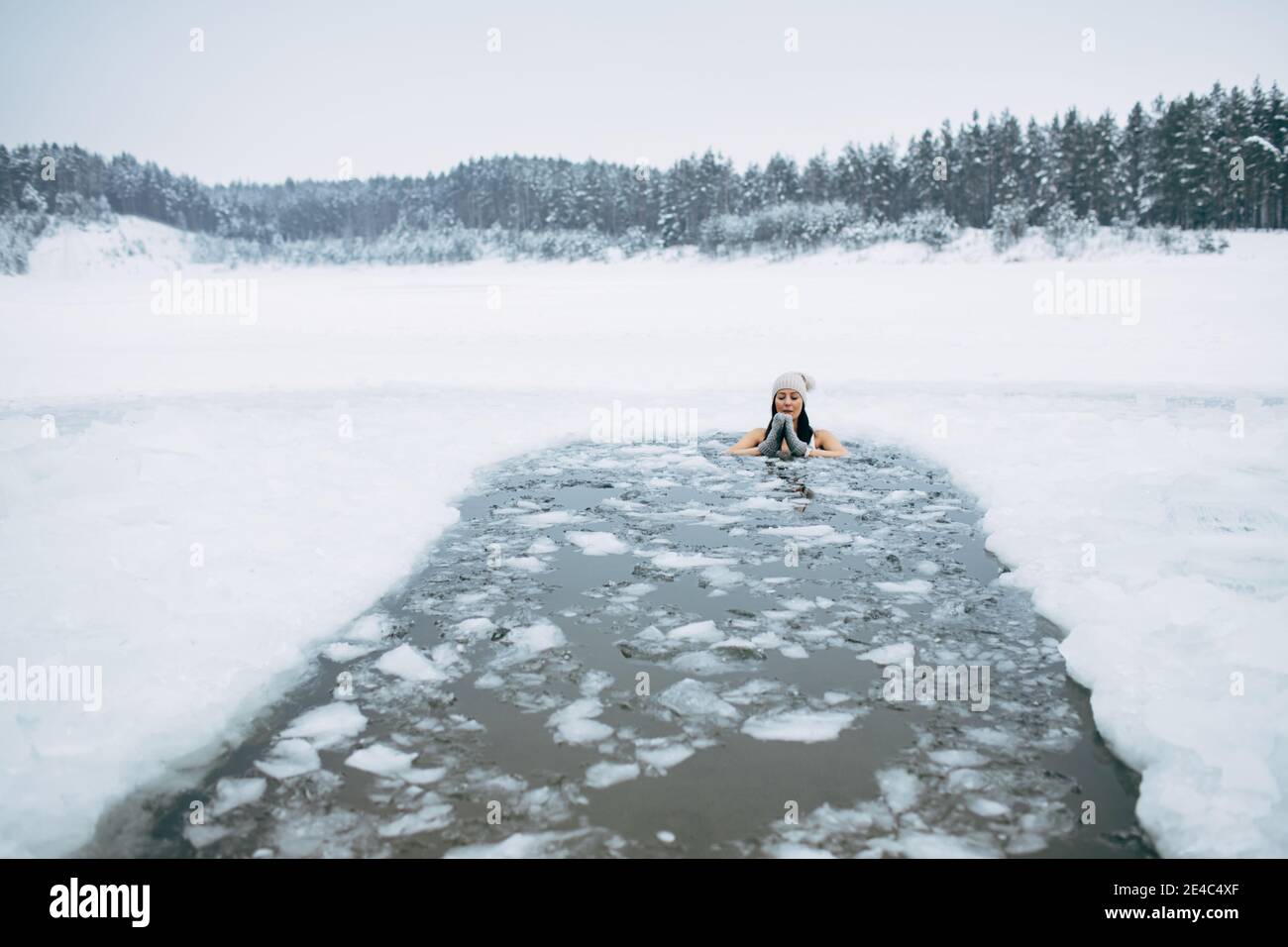 Natation en hiver. Femme dans un trou de glace de lac gelé. Bien-être des nageurs dans l'eau glacée. Comment nager dans l'eau froide. Belle jeune femme en méditation zen. Banque D'Images