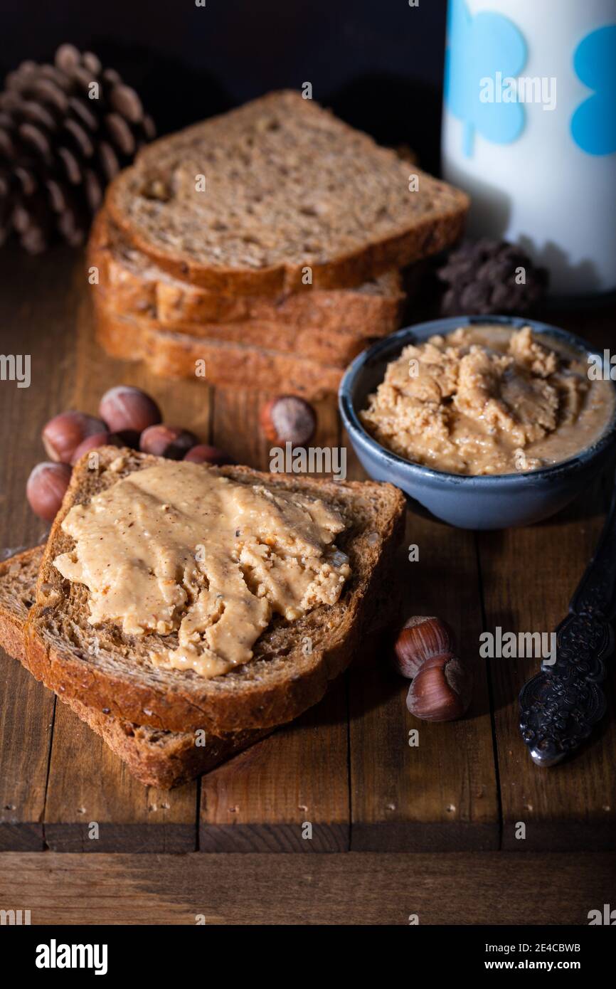 Tranches de pain avec tartinade aux noisettes maison et verre de lait sur table en bois. Beurre aux noisettes maison. Banque D'Images