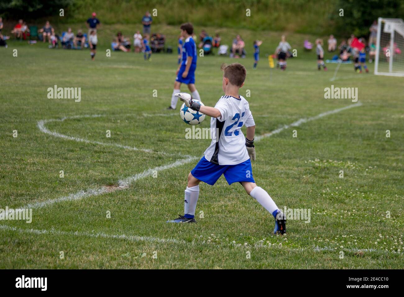 Un garçon qui donne un coup de pied au ballon de football de sa zone finale à la fin de la ligue des jeunes. Banque D'Images