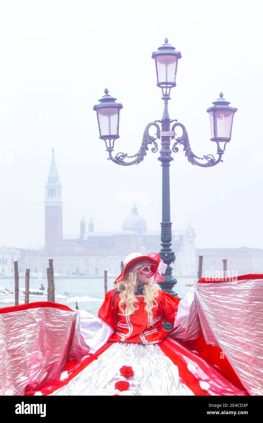 Italie, Vénétie, Venise, femme en costume rouge au carnaval de venise, matin brumeux dans la lagune vénitienne Banque D'Images