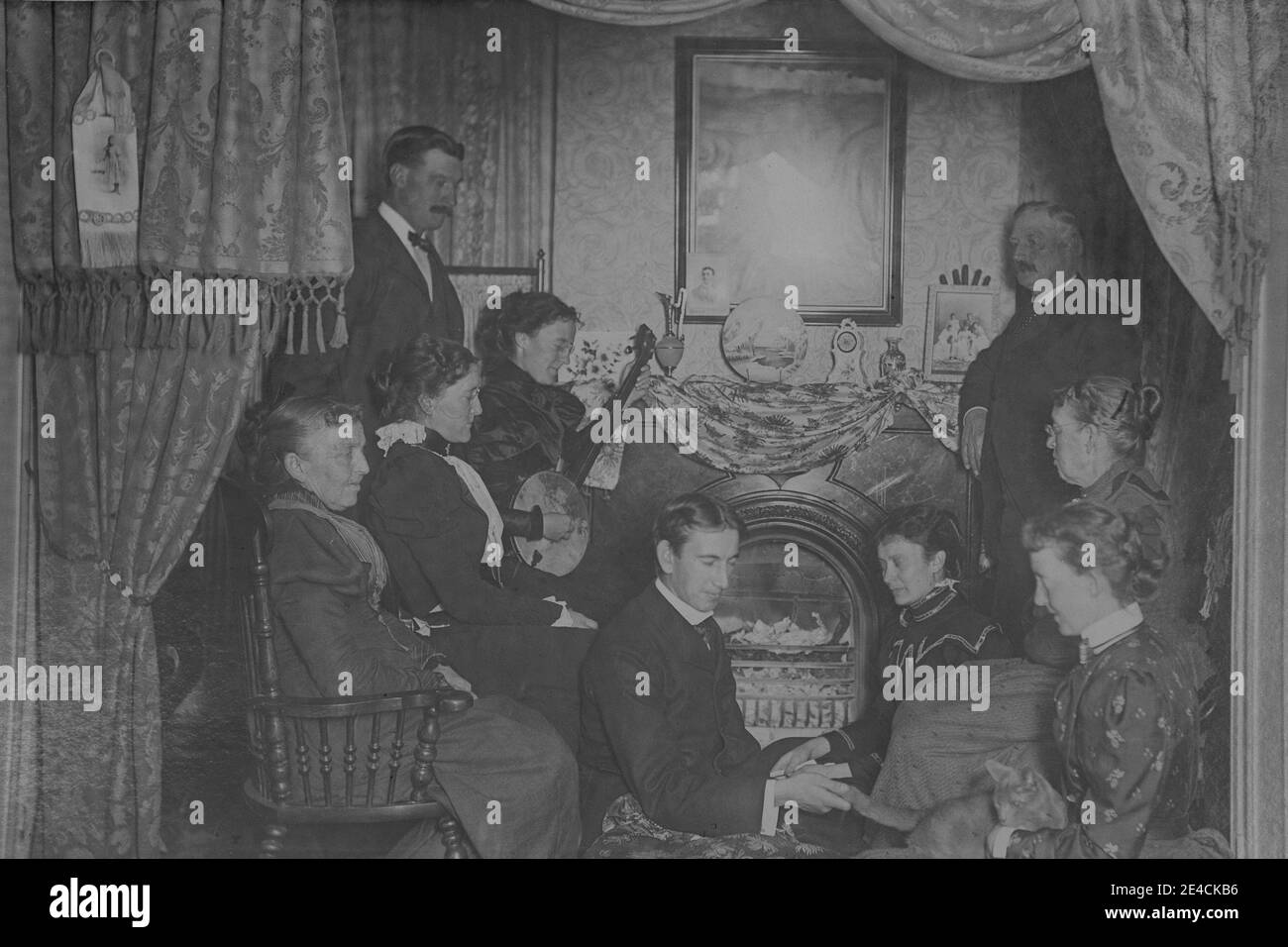American archive monochrome portraitof un groupe de personnes à la maison appréciant le divertissement. Une femme joue un banjo. Prise à la fin du XIXe siècle à Byron, NY, États-Unis Banque D'Images