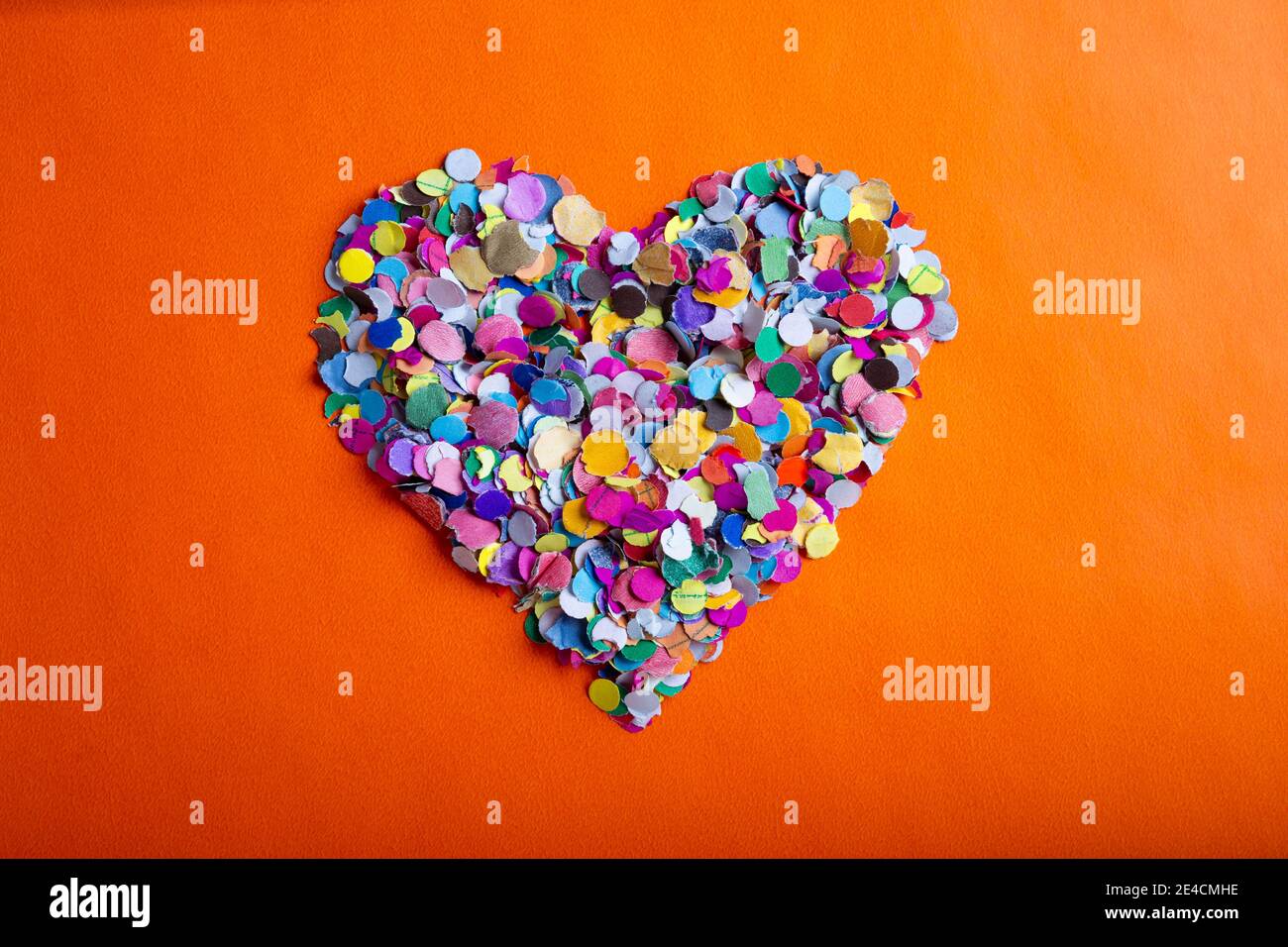 image de concept d'amour de la forme de coeur en confettis colorés sur fond de texture de papier orange Banque D'Images