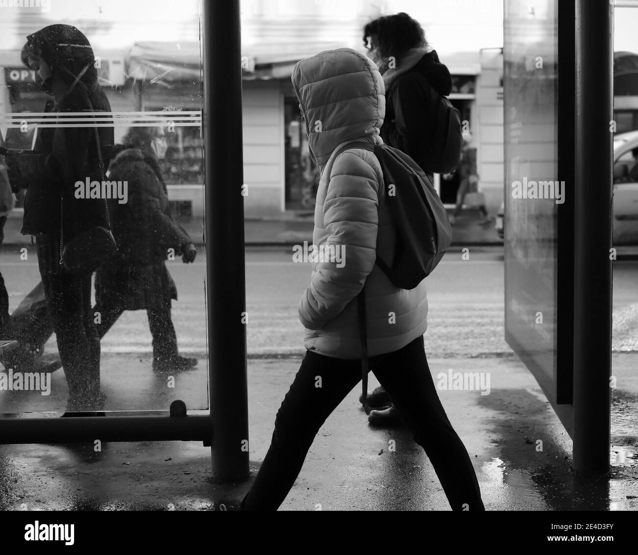 Scène urbaine avec une fille à capuchon passant devant l'arrêt de bus (N/B) Banque D'Images