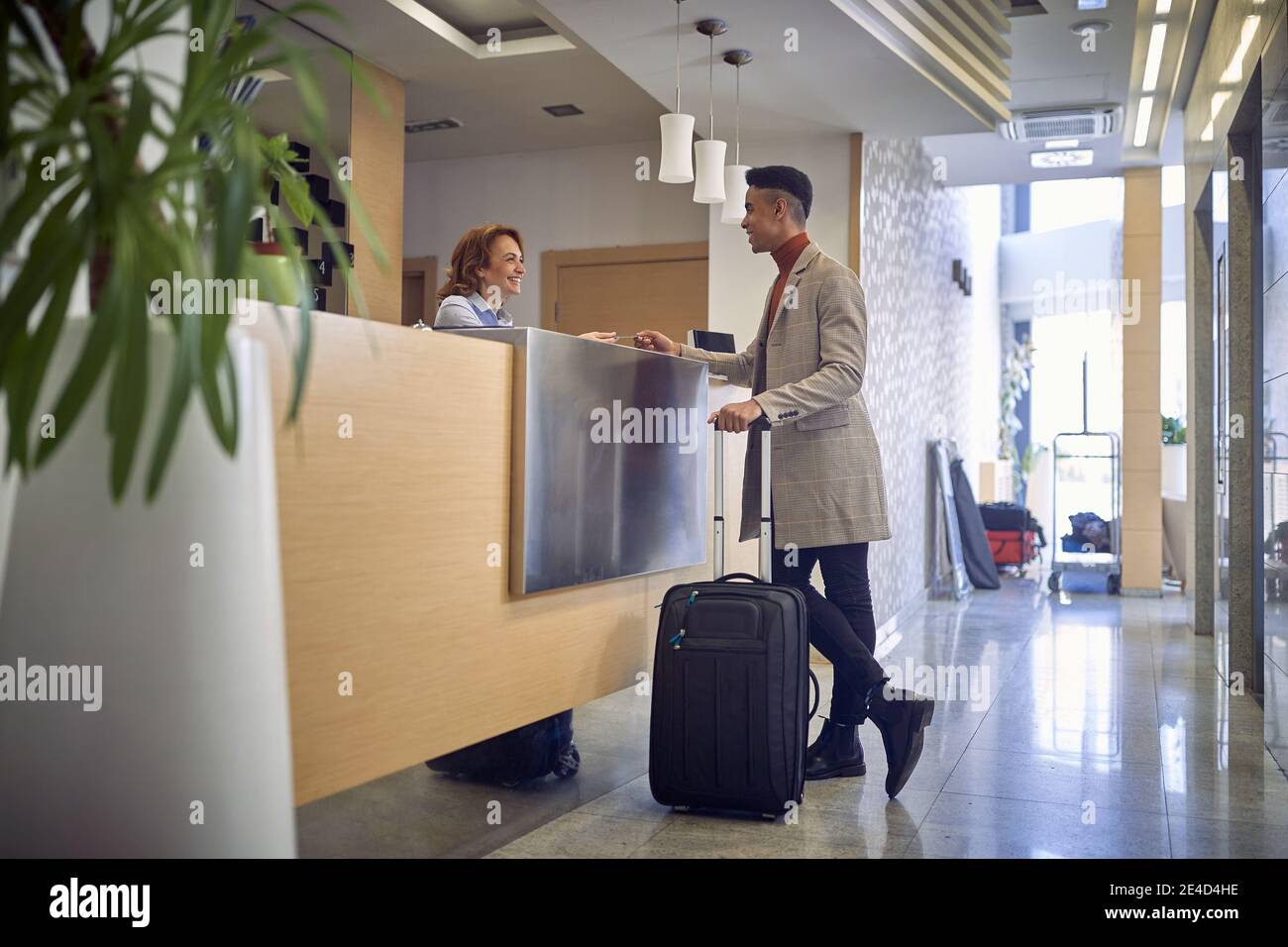 jeune afro-américain payant avec une carte à une femme amicale caucasien à la réception à l'entrée de l'hôtel Banque D'Images