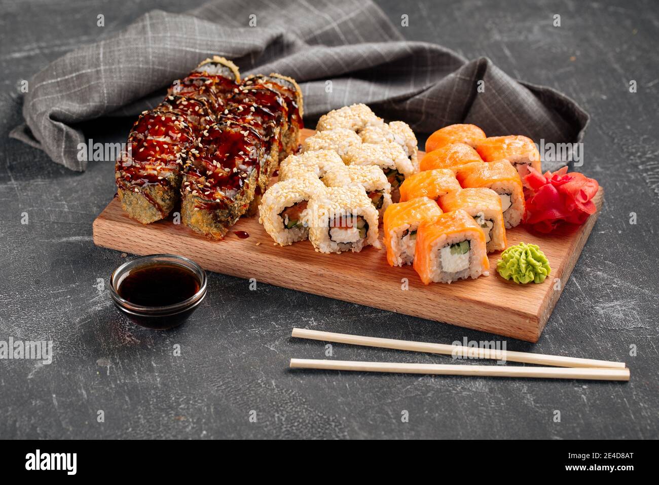 Vue latérale sur un assortiment de petits pains à sushis sur une planche de bois avec de la sauce au wasabi et au soja Banque D'Images