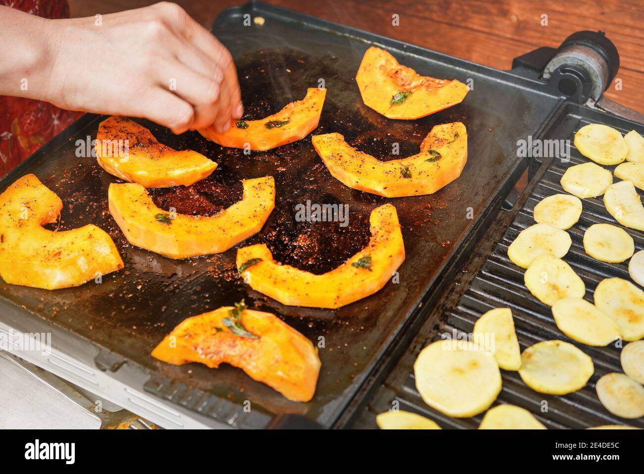 Courge de noyer cendré orange vif grillée sur le gril électrique, femme floue main déplaçant des morceaux de légumes sur la plaque chaude Banque D'Images