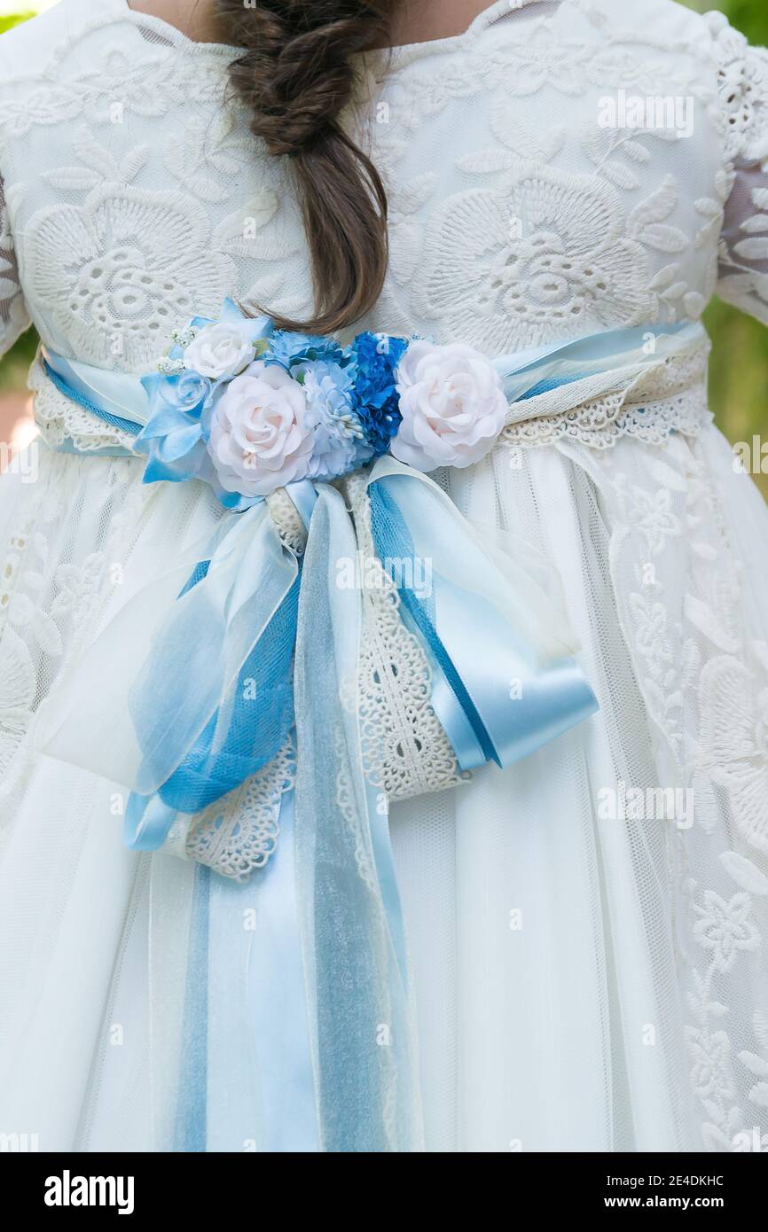 Dentelle texturée au dos de la robe blanche d'une fille avec noeud et fleurs bleues. Banque D'Images