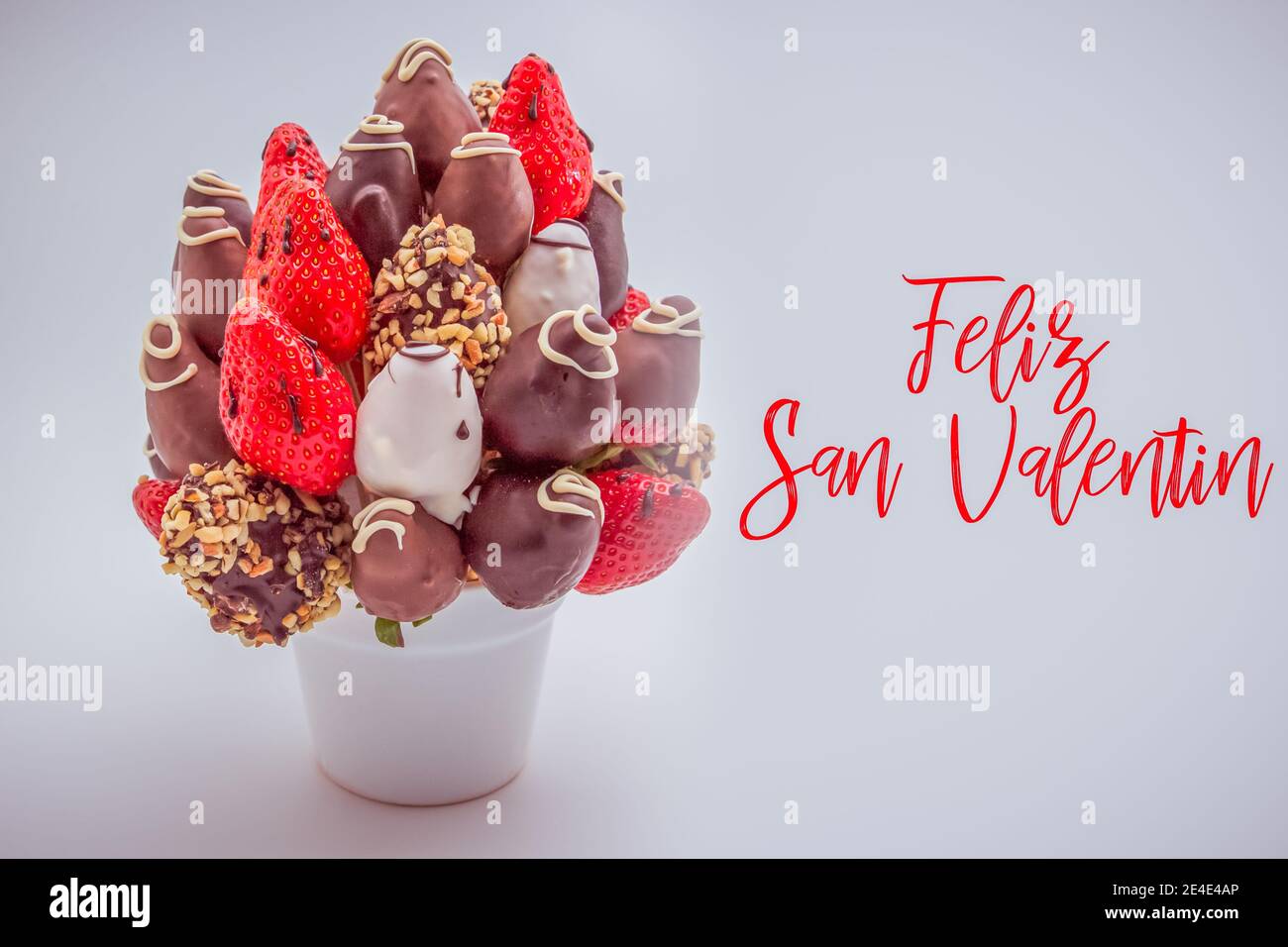 Carte de vœux de bonne Saint Valentin en espagnol avec des lettres rouges qui lit Feliz San Valentin; bouquet de fleurs comestibles, arrangement de trempette au chocolat Banque D'Images