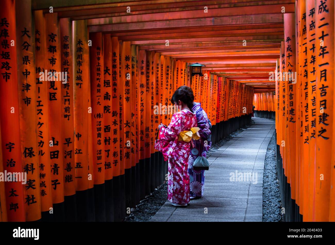 Deux adolescents au milieu de la porte de Torii en bois rouge au sanctuaire de Fushimi Inari à Kyoto, au Japon. Accent sélectif sur les femmes portant un kimono japonais traditionnel. Banque D'Images