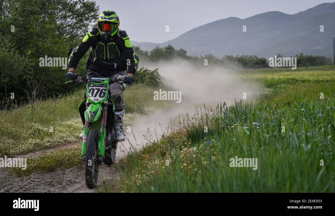 Un motocross de kawasaki conduit sur une route de terre surcultivée avec de l'herbe et des plantes et un nuage de poussière s'élève derrière lui. Banque D'Images