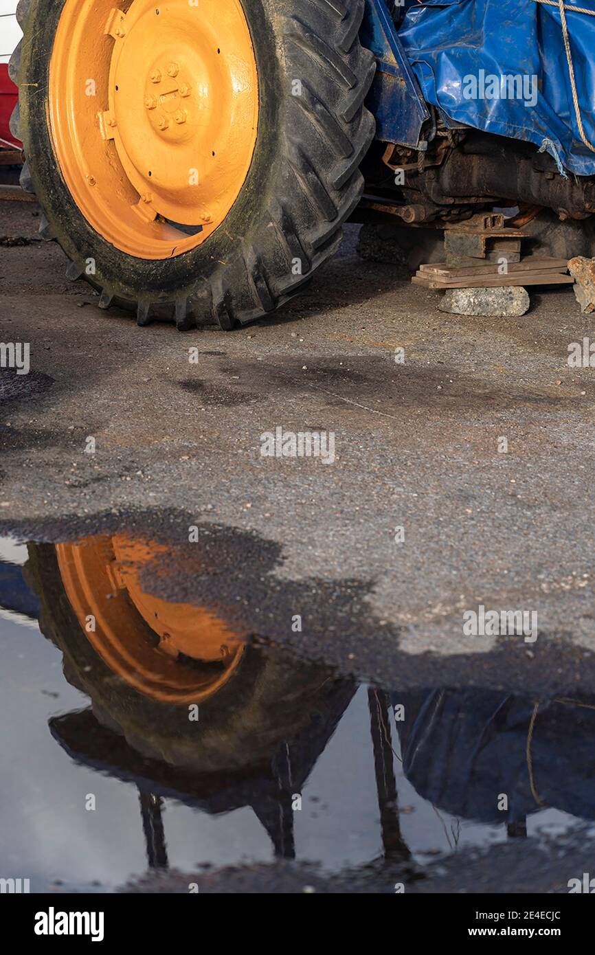 roue jaune du tracteur reflétée dans la flaque de pluie Banque D'Images